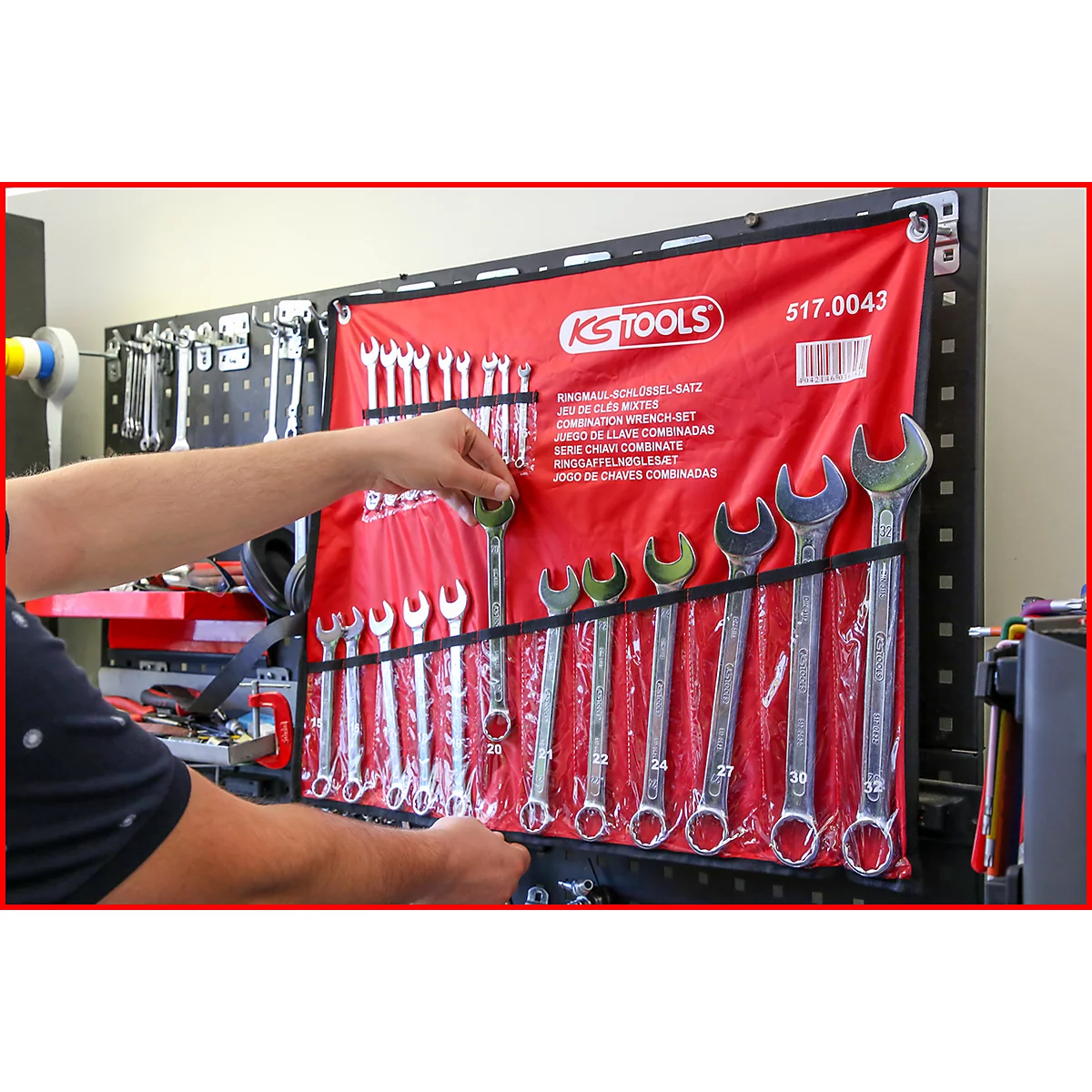 Ein Mann entnimmt einen Schraubenschlüssel aus einer roten Werkzeugrolle. Darin befinden sich weitere Schlüssel.